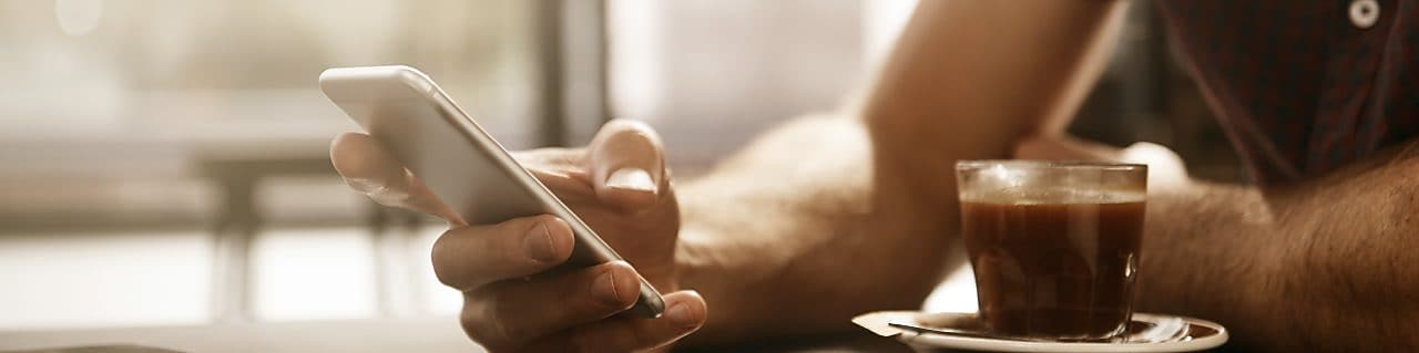 Άνδρας πίνει έναν καφέ και χρησιμοποιεί ένα smartphone