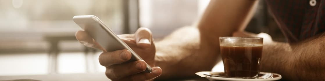 Άνδρας πίνει έναν καφέ και χρησιμοποιεί ένα smartphone