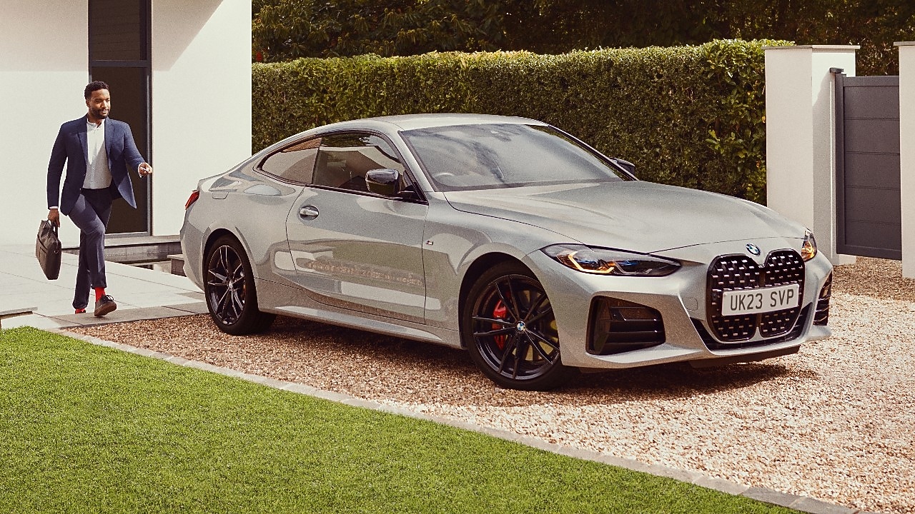 Μια λευκή BMW M3 σταθμευμένη σε μια διαδρομή με έναν άνδρα να περπατά προς το μέρος της – λευκό σπίτι στο βάθος