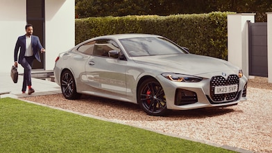 Μια λευκή BMW M3 σταθμευμένη σε μια διαδρομή με έναν άνδρα να περπατά προς το μέρος της – λευκό σπίτι στο βάθος
