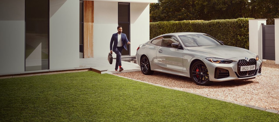 Μια λευκή BMW M3 σταθμευμένη σε μια διαδρομή με έναν άνδρα να περπατά προς το μέρος της – λευκό σπίτι στο βάθος